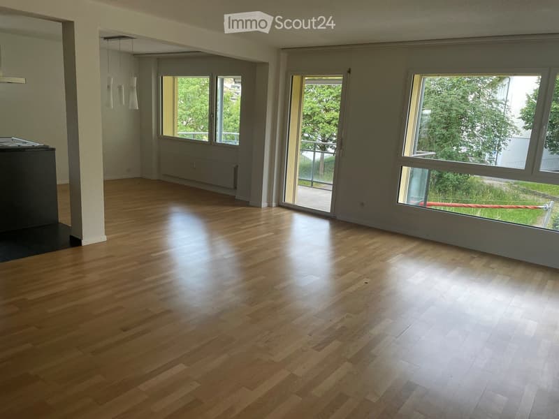 Empty room with wooden flooring, large windows, and sliding glass doors leading to a balcony.