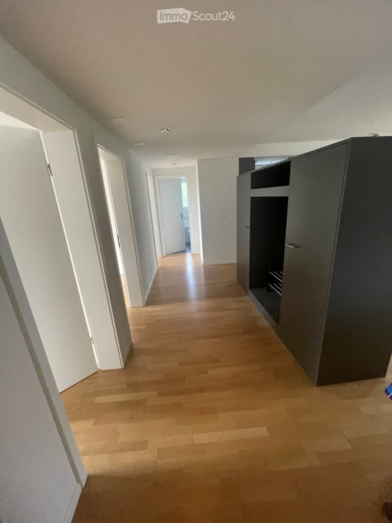 Empty hallway with wooden flooring, white walls, and several doors leading to other rooms.