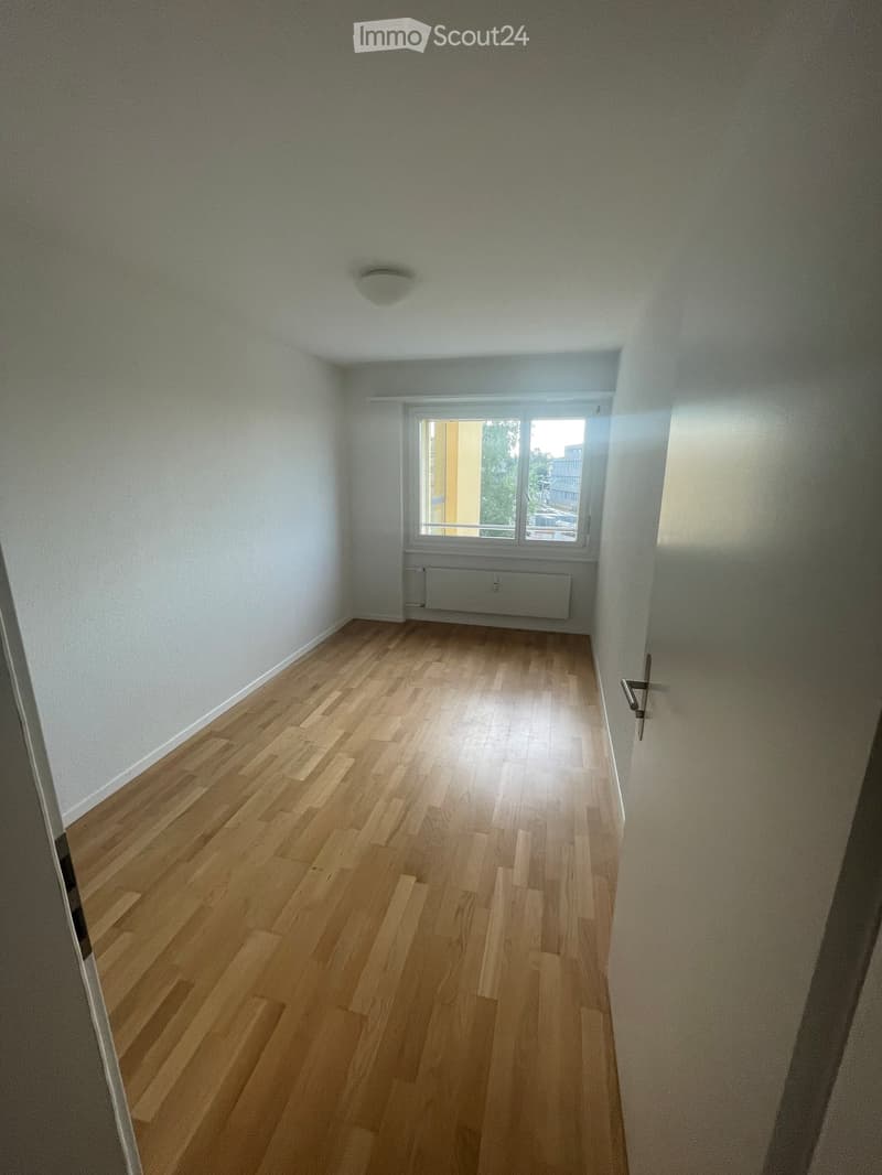 Empty room with light wooden flooring, white walls, and a single window with a radiator below it.