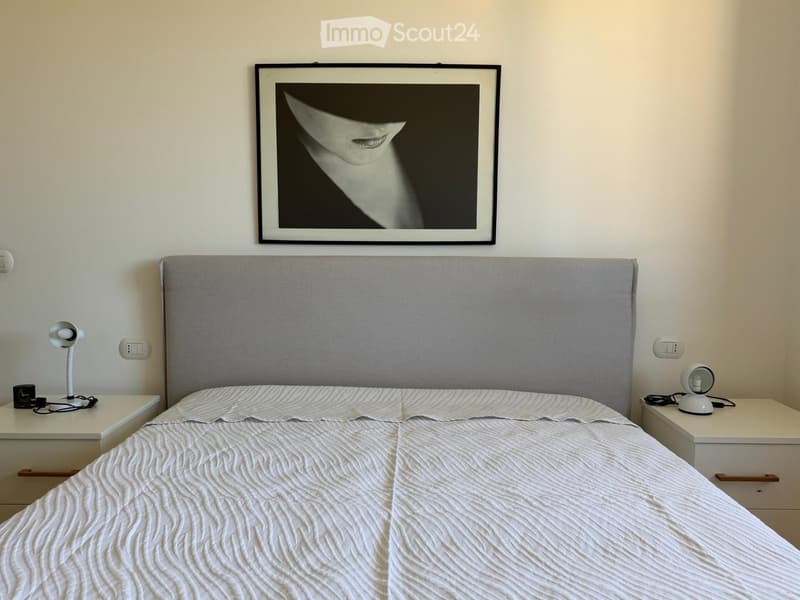 Modern bedroom with a large bed, grey headboard, nightstands, lamps, and a framed picture on the wall.