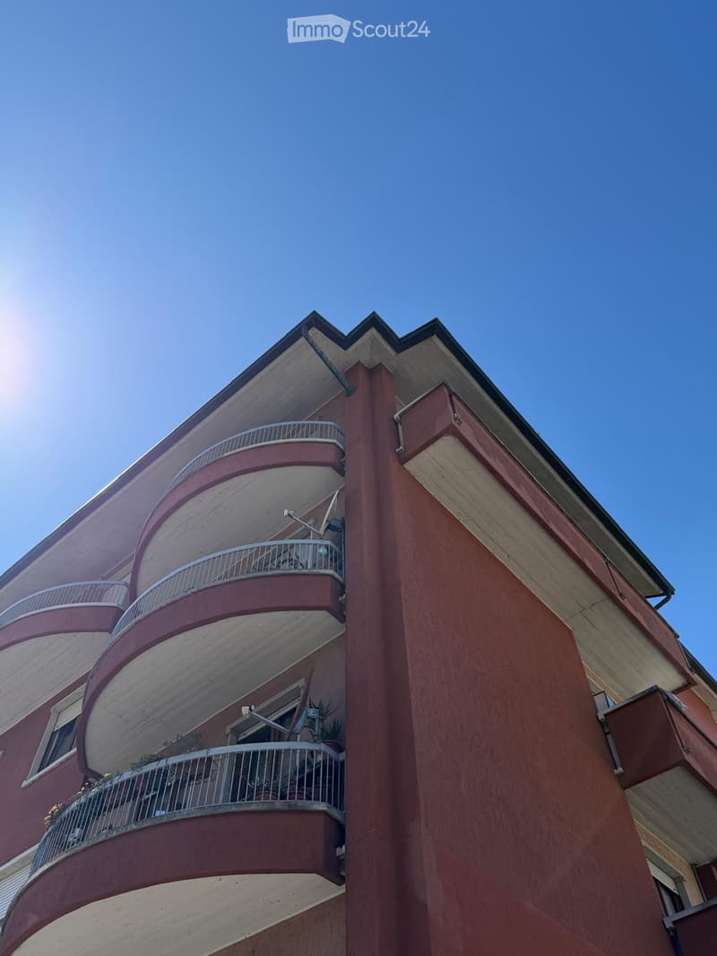 Multi-story residential building with red brick facade, curved balconies, and metal railings.