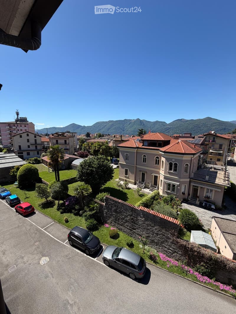 Aerial view of a residential area with multiple houses, parked cars, and a scenic mountain backdrop.