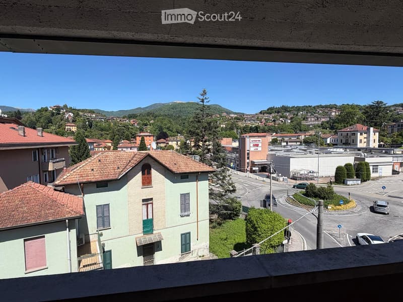 Balcony view overlooking a town with houses, trees, and distant mountains under a clear blue sky.