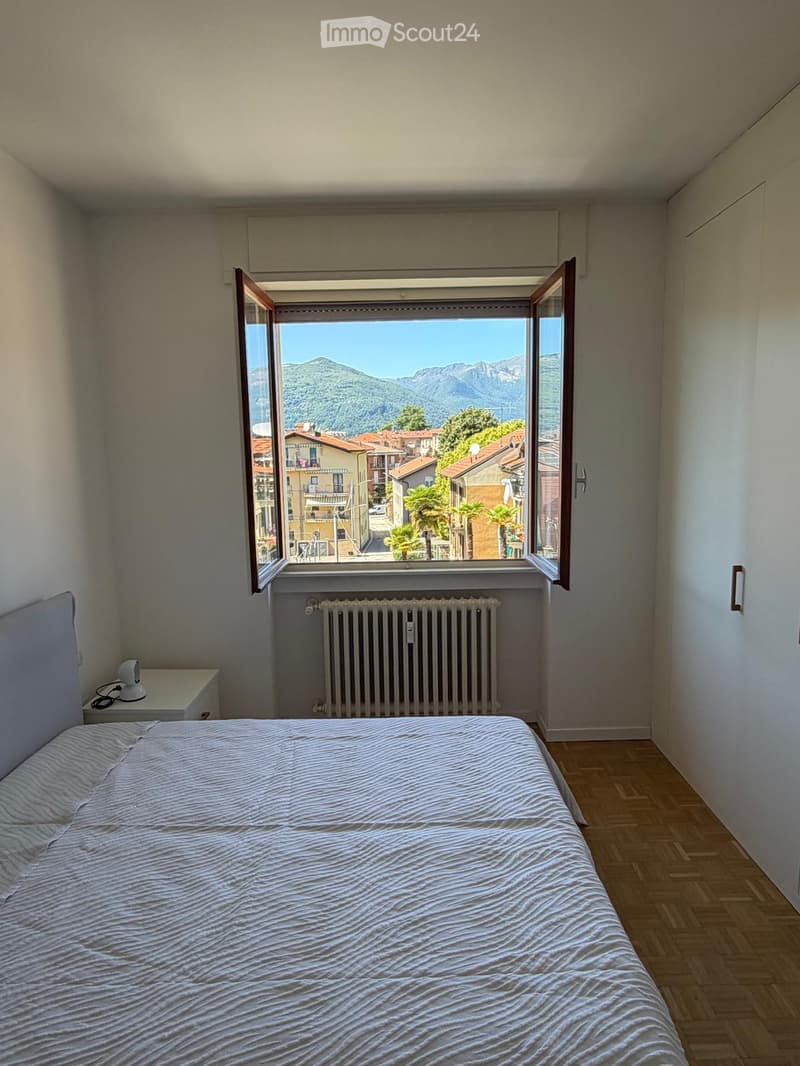 Bedroom with a single bed, nightstand, radiator, and large window offering a scenic mountain view.