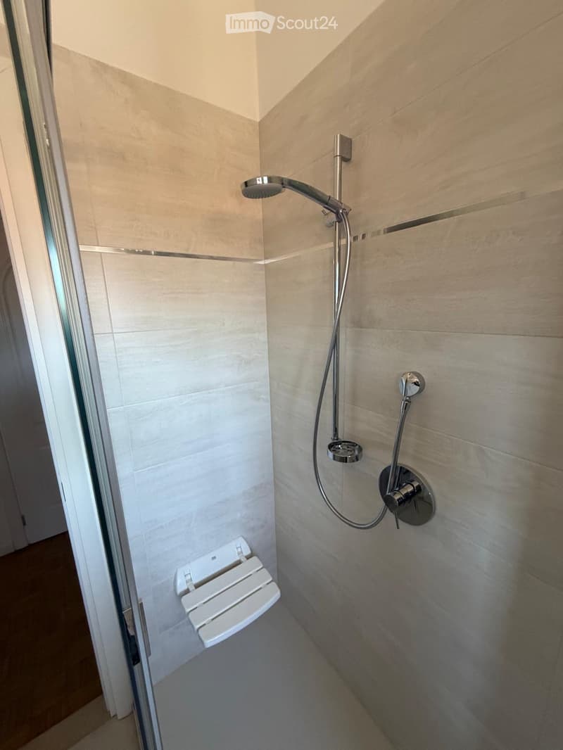 Modern shower area with light-colored tiles, a handheld showerhead, a fixed showerhead, and a built-in shower seat.