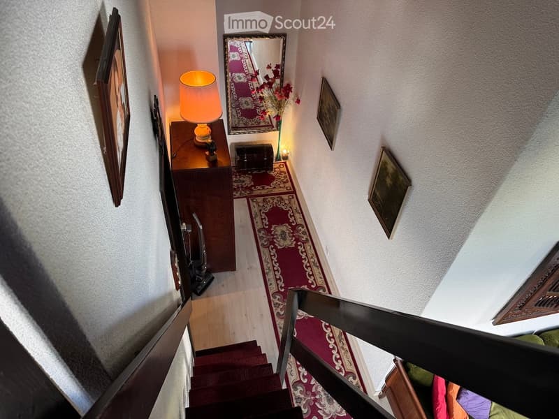 Staircase with wooden steps and red carpet runner, small table with lamp, mirror, and framed artwork on walls.