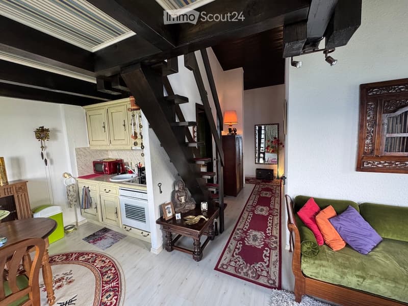 Cozy living and dining area with a green sofa, wooden coffee table, dining table, kitchen area with cabinets and microwave, staircase leading to another level, and decorative items including a mirror and lamp.