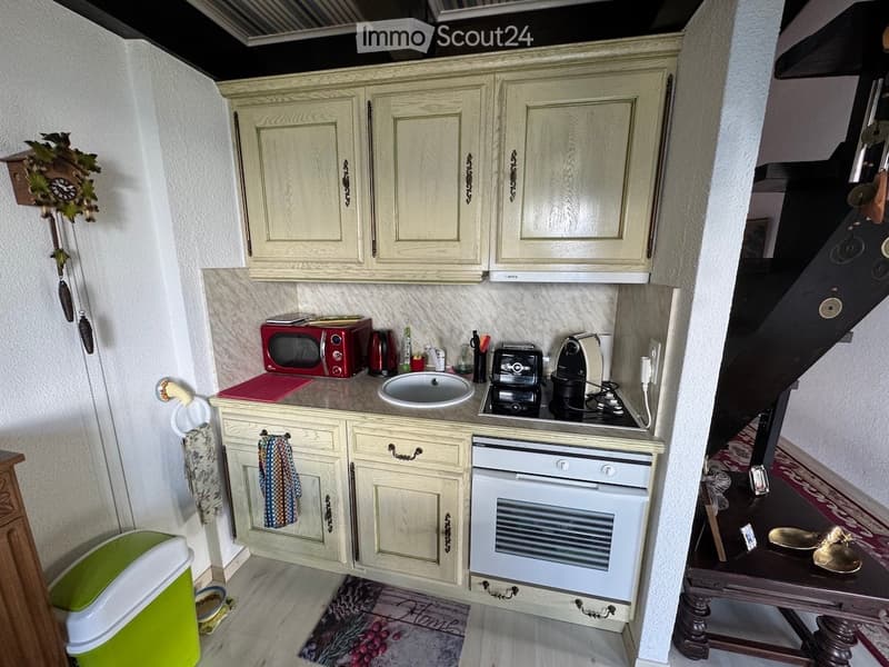 Compact kitchen with light-colored cabinets, microwave, oven, coffee maker, toaster, sink, and a small countertop area.