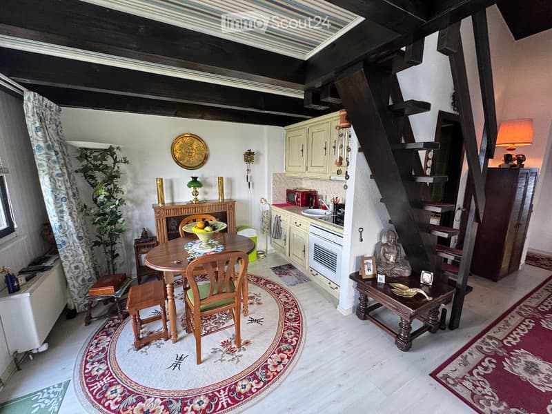A cozy, well-furnished room with a dining area, kitchen, and living space. Features include a wooden dining table with chairs, a kitchen area with cabinets, sink, oven, and microwave, a small living area with a coffee table and decorative items, and a sta