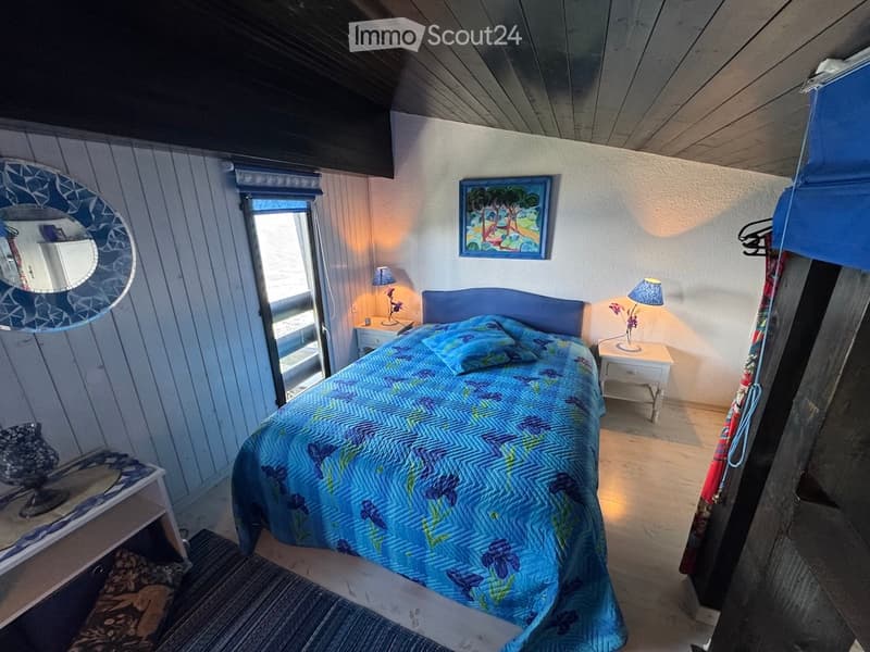 Cozy bedroom with a double bed, nightstands, lamps, a mirror, and a picture frame on the wall. The room features wooden walls and a view through a large window.