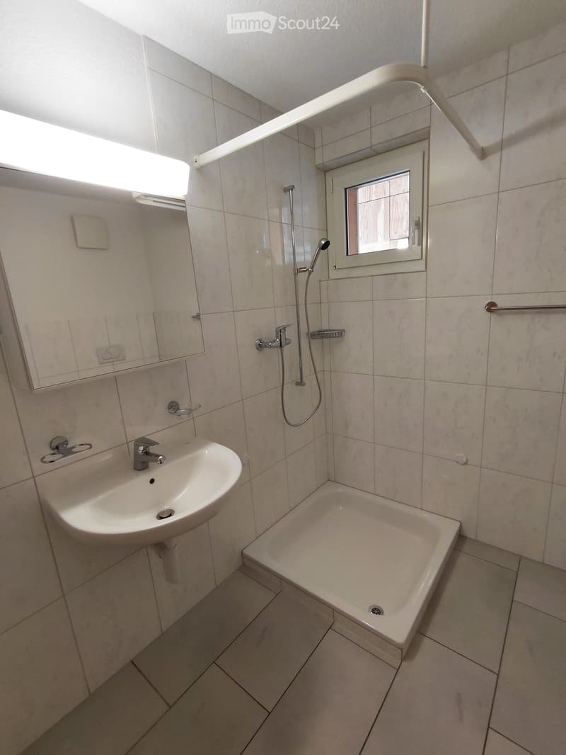 Modern bathroom with a white tiled design, featuring a sink, bathtub, showerhead, and a mirror above the sink.