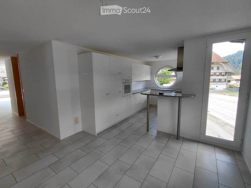 Modern kitchen with white cabinetry, stainless steel appliances, and a central island. Features a large window and a round porthole window above the sink.