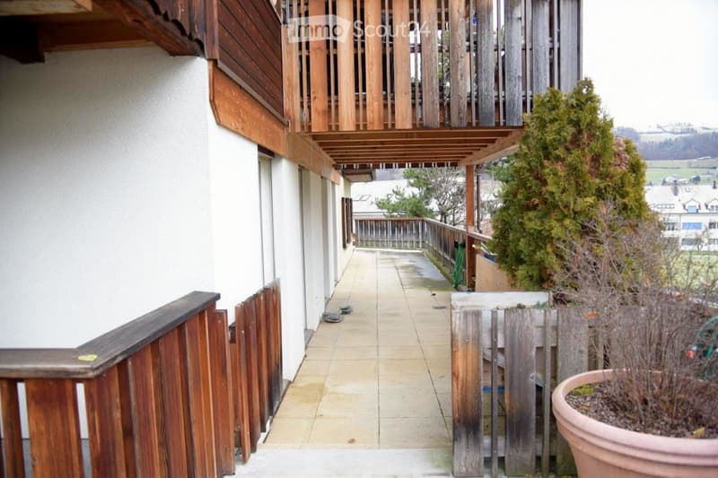 Balcony with wooden railings, tiled floor, and potted plants, overlooking a residential area with houses and trees.
