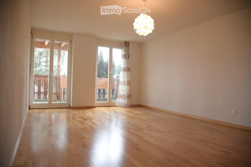 Empty room with wooden flooring, large windows, and a hanging light fixture. No furniture or equipment present.