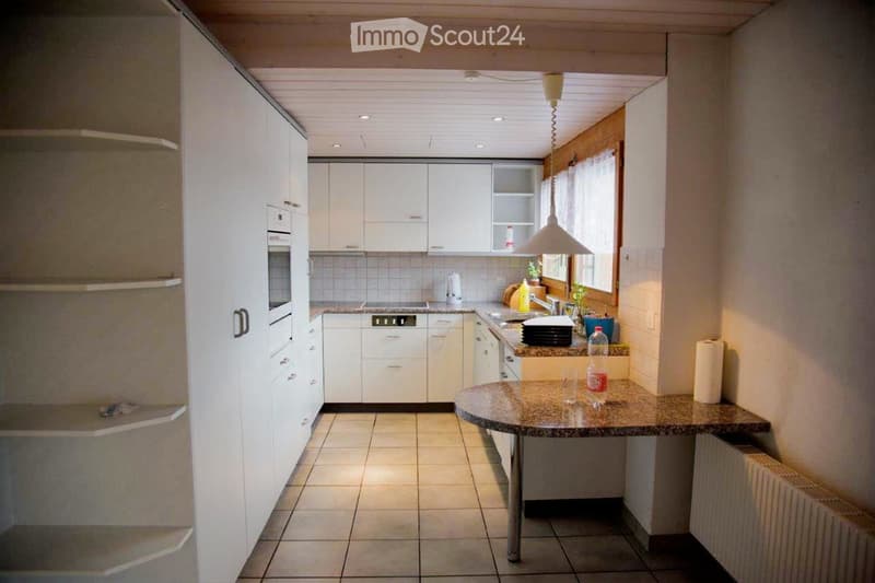 Modern kitchen with white cabinets, granite countertops, and stainless steel appliances. Features an island with a round table and various kitchen items.