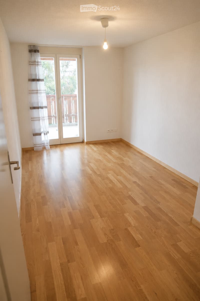 Empty room with wooden flooring, white walls, and a sliding glass door leading to a balcony.