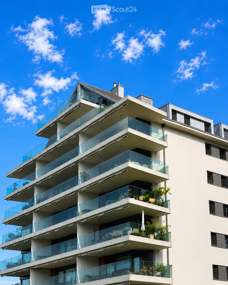 Modern multi-story residential building with multiple balconies featuring glass railings and potted plants, under a clear blue sky.