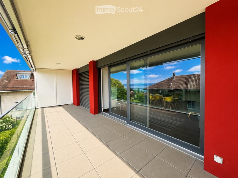 Modern balcony with large glass sliding doors, tiled floor, and a view of the surrounding landscape and neighboring buildings.