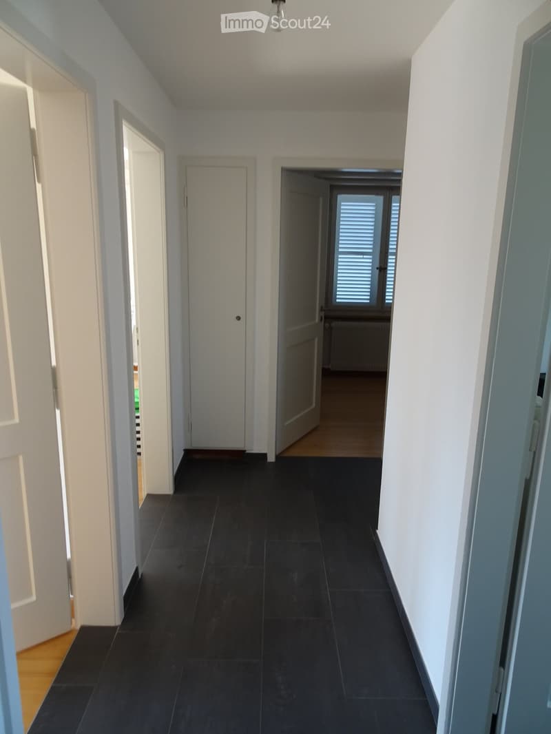 Empty hallway with dark tiled flooring, white walls, and several doors leading to other rooms.