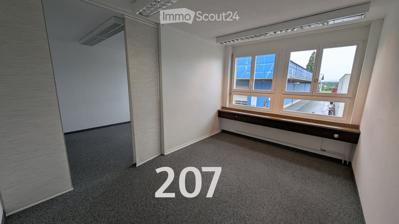 Empty room with grey carpet, white walls, large windows, and a small built-in desk unit.