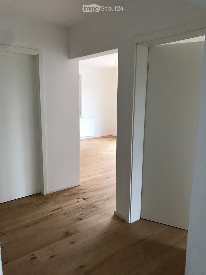 Empty room with light wooden flooring and white walls, featuring an open doorway leading to another room.