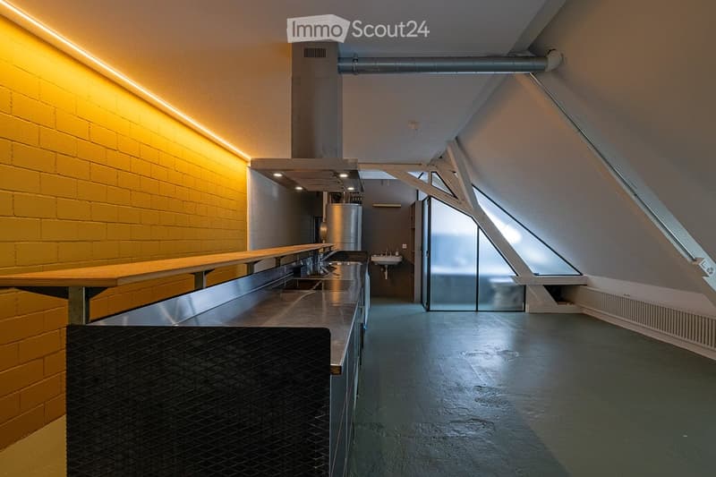 Modern hallway with exposed brick wall, sleek stainless steel counter, and industrial-style lighting. Features a small sink area and a large window at the end.