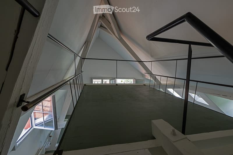 Modern, open staircase with glass railings and wooden beams, leading to an upper level with large windows providing natural light.