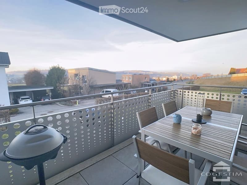 Balcony with a view, featuring a small table with chairs, a teapot, a cup, and a candle. The railing has a decorative perforated metal design.