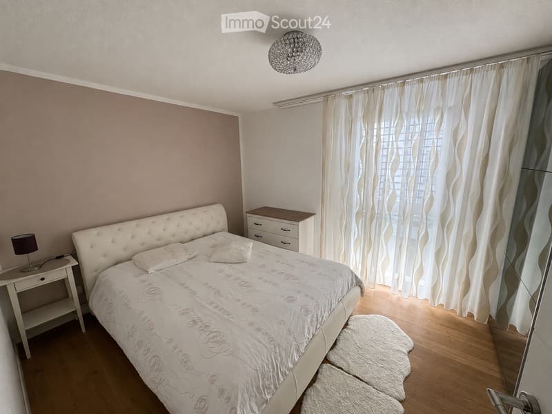 Modern bedroom with a tufted headboard bed, white bedding, nightstands, lamps, and a large window with sheer curtains.