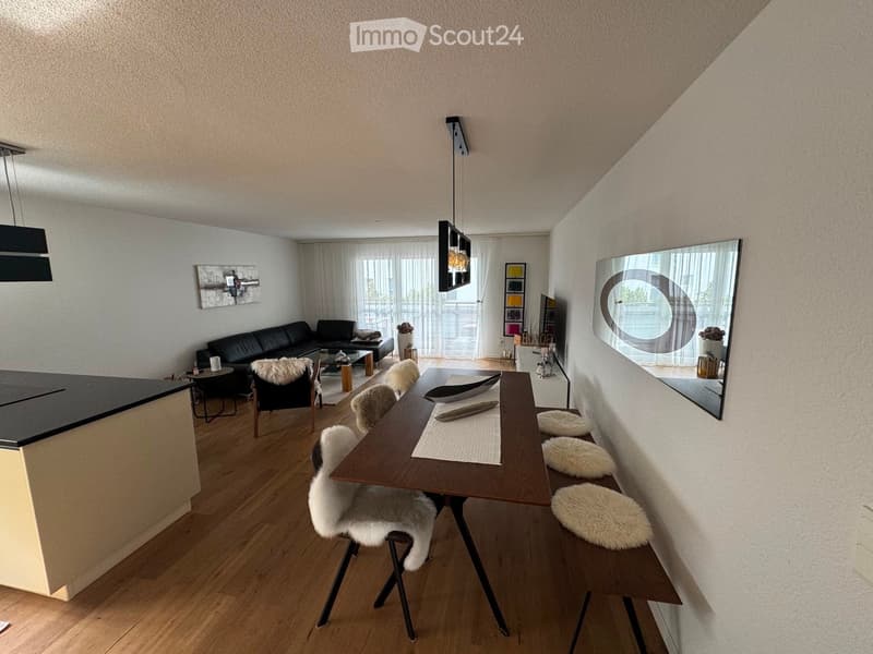 Modern open-plan living and dining area with a black leather sofa, coffee table, dining table with chairs, and a large mirror on the wall.