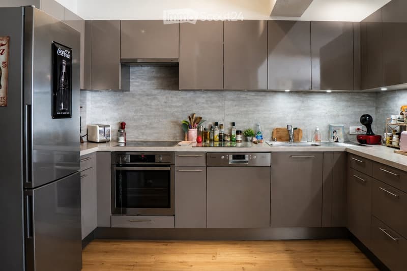Modern kitchen with grey cabinets, stainless steel appliances, and a marble backsplash. Features include a refrigerator, oven, dishwasher, toaster, sink, and various kitchen utensils and items on the counter.