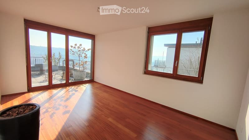 Empty room with wooden flooring, large windows, and sliding glass doors leading to a balcony.