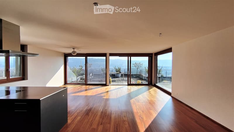 Open-concept space with wooden flooring, large windows, and sliding glass doors leading to a balcony or outdoor area. The room is empty, with no furniture or furnishings visible.