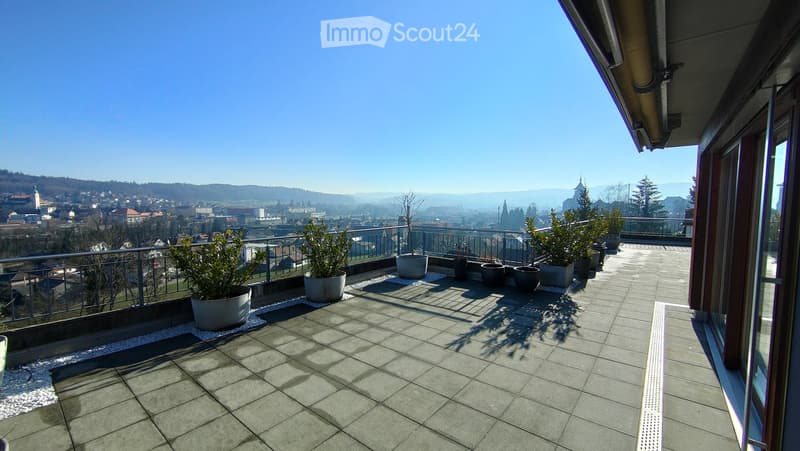 Balcony with tiled floor, metal railing, and potted plants, offering a panoramic city view.