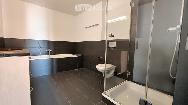 Modern bathroom with dark tiled walls and floor, featuring a bathtub, toilet, glass-enclosed shower, and a sink with a faucet.