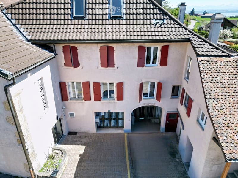 Two-story house with beige walls, red shutters, and a tiled roof. Features a small entrance area with a gate and a paved pathway.