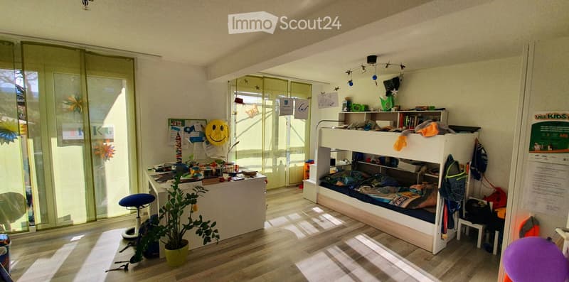 A well-lit room with a bunk bed, a small table with a plant, a stool, and various decorations including a smiley face balloon and artwork on the walls.