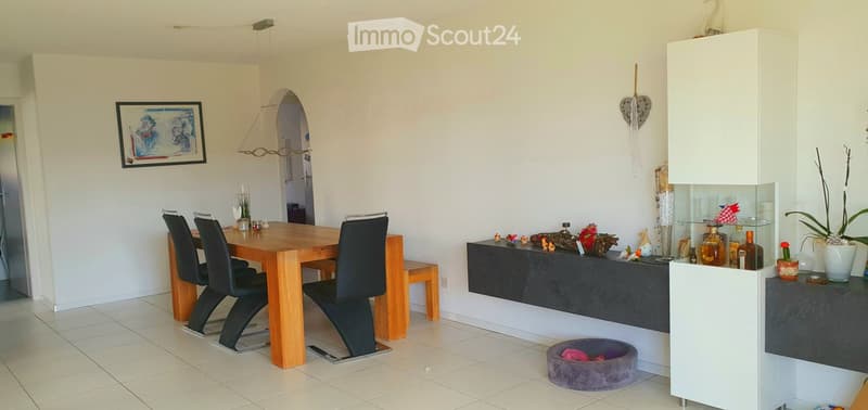 Modern dining area with a wooden dining table, black chairs, a white cabinet, decorative bottles, and a vase on the counter.