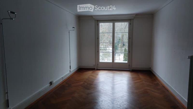 Empty room with wooden herringbone flooring, white walls, and a large glass door leading to a balcony or outdoor area.