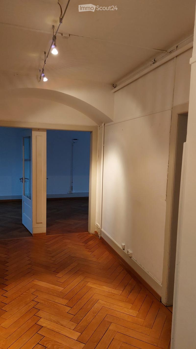 Empty hallway with wooden herringbone flooring, white walls, and two open doors leading to other rooms.