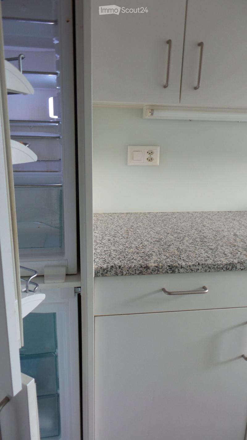A modern kitchen with light grey cabinets, a granite countertop, and an open refrigerator showing shelves and drawers.