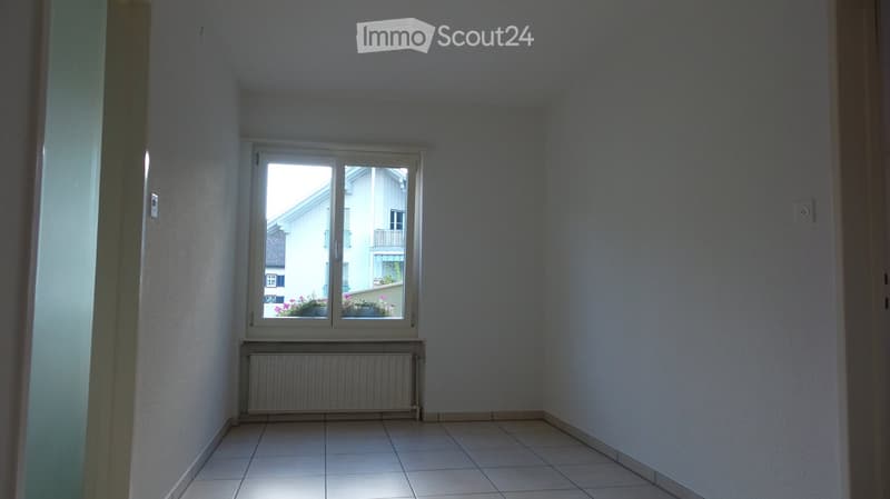 Empty room with tiled floor, white walls, a window with a radiator below, and a view of neighboring buildings.