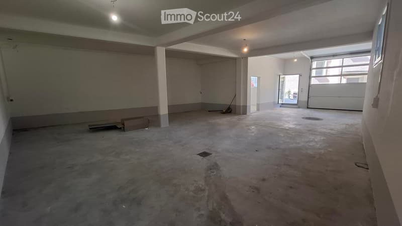 Empty room with concrete floor, white walls, and large garage door opening to an outdoor area.