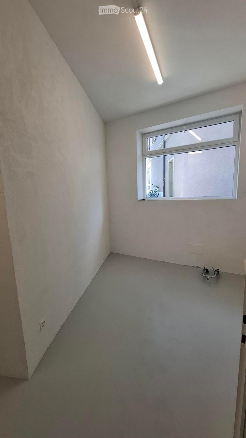 Empty room with light-colored walls, grey carpeted floor, and a single window showing a view of a bicycle outside.