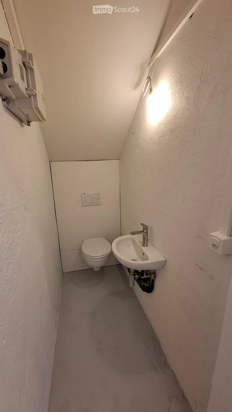 Compact bathroom with a toilet and a sink, featuring white walls and a light fixture on the wall.