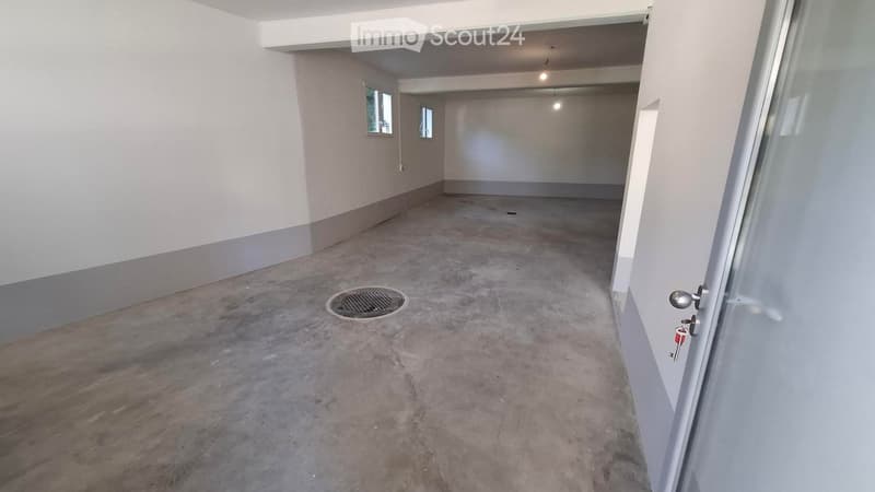 Empty room with concrete floor, white walls, small windows, and a drain cover in the center.