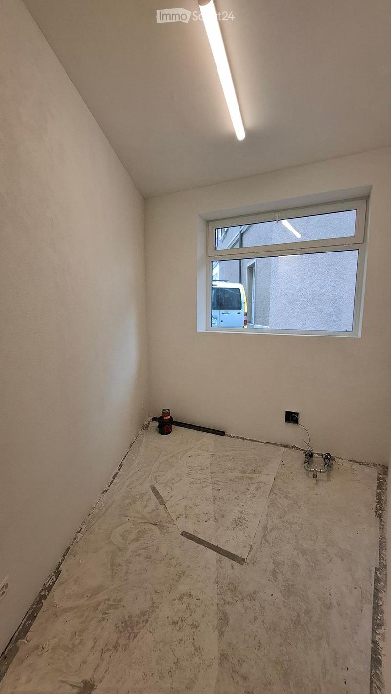 Empty room with bare walls and unfinished floor, featuring a single window and exposed electrical wiring.