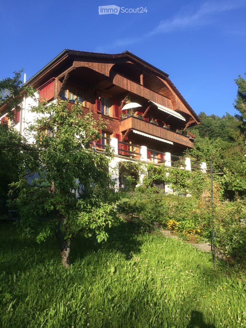 A two-story wooden house with red shutters, balconies, and a well-maintained garden.