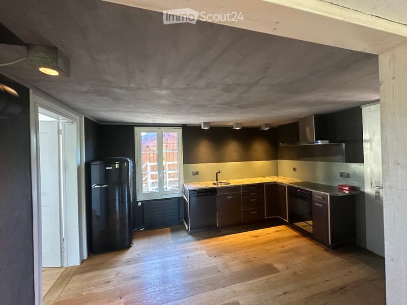 Modern kitchen with wooden flooring, dark cabinets, stainless steel appliances, and a window overlooking a wooden deck.