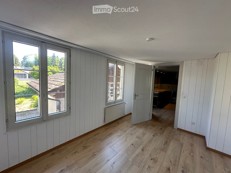 Empty room with wooden flooring, white walls, large windows, and an open door leading to another room.